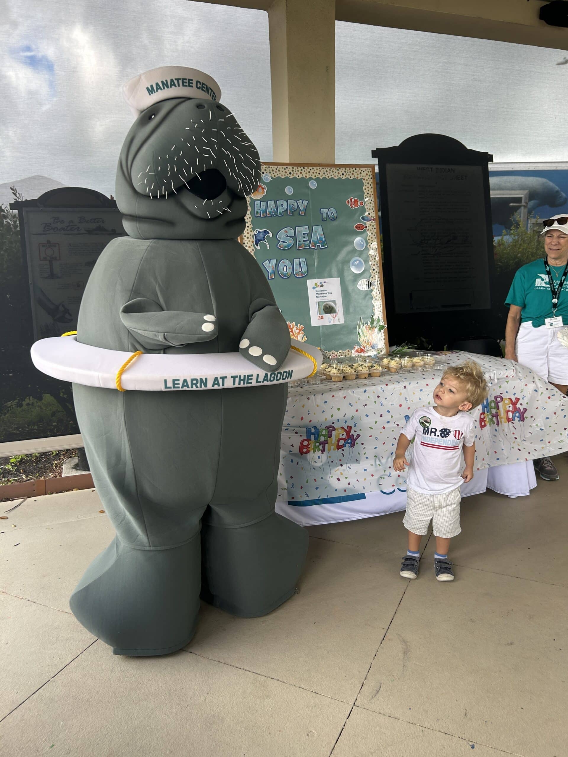 young boy standing next to manatee in costume